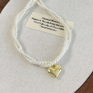 Vue détaillée d'un collier de perles double couche avec un grand pendentif cœur doré