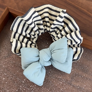 Detail of striped scrunchie with blue bow on a textured tray for bun hairstyles