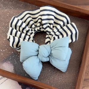 Detail of striped hair scrunchie featuring a puffy light blue bow on a wooden tray
