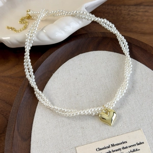 Gros plan sur un collier de perles double épaisseur avec pendentif cœur doré sur plateau