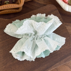 Detail of mint green hair scrunchie with white embroidery lace on a wooden board