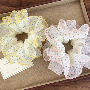 Détail de chouchous surdimensionnés en mousseline fleurie jaune et rose sur un plateau