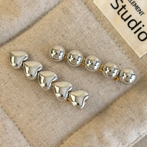 Détail de barrettes en métal argenté à cœurs et billes sur un fond en lin beige clair