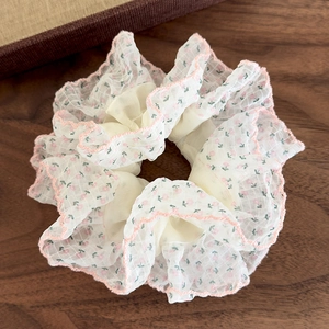 Détail d'un chouchou en organza fleuri avec bords brodés roses sur table en bois sombre