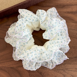 Détail d'un chouchou crème à motifs floraux bleus et broderies ondulées violettes