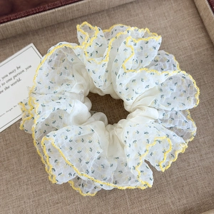 Vue macro détaillée d'un chouchou en organza ivoire avec motifs floraux jaunes et bords ondulés