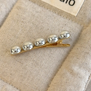 Détail de billes argentées sur pince à cheveux dorée posée sur un tissu en lin