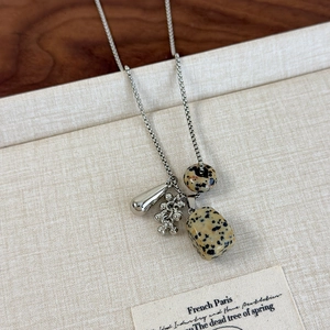 Detail view of natural spotted stone pendant and silver water drop charm on long necklace