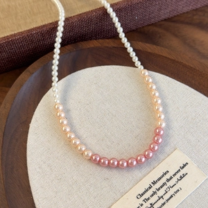 Detailed view of elegant gradient white and pink pearl necklace on a rustic wooden tray
