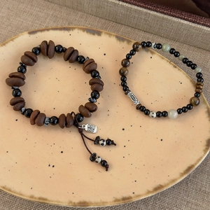 Tiger eye and coffee bean bead bracelets with silver Fu pendant on ceramic plate