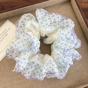 Détail d'un chouchou en organza floral avec imprimés bleus et bordure ondulée mauve