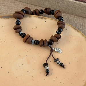 Macro detail of coffee bean bracelet featuring a silver Fu charm on a rustic ceramic plate