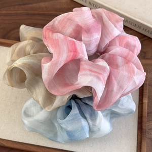 Détails des chouchous en mousseline tie-dye rose, bleu et beige sur un plateau en bois