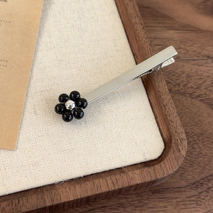 Detailansicht der silbernen Haarklammer mit einer schwarzen Perlenblüte auf Struktur
