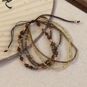 Macro detail of Bohemian multilayer beaded bracelets in earth tones on a linen background