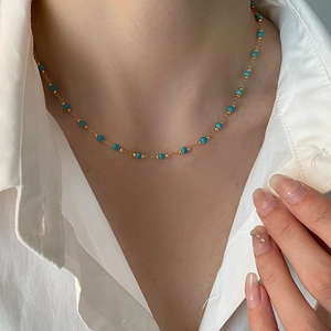 Bohemian gold chain necklace with turquoise beads worn on a model in a white shirt