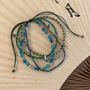 Detail of layered bohemian beaded bracelets with crystal pendants on a cream folding fan