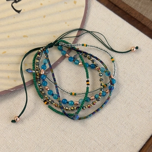 Detail of layered bohemian beaded bracelet with emerald and gold tones on a woven mat