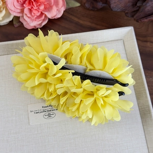 Gros plan sur la pince à cheveux fleur en mousseline jaune avec base banane noire