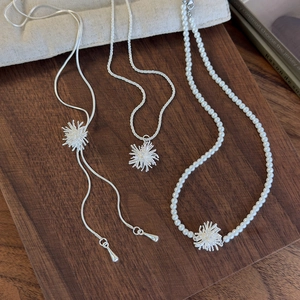Detailed view of silver firework starburst pendants with pearls on titanium steel necklaces