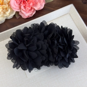 Gros plan sur la pince à cheveux double fleur en mousseline noire sur fond beige