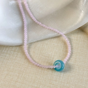 Detailed macro of pink crystal beads with translucent green donut charm on silk fabric