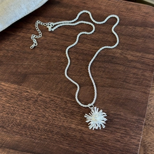 Detail of silver firework starburst pendant with textured chain on wooden surface
