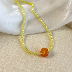 Detailed close-up of yellow faceted crystal beads and orange agate pendant on satin fabric