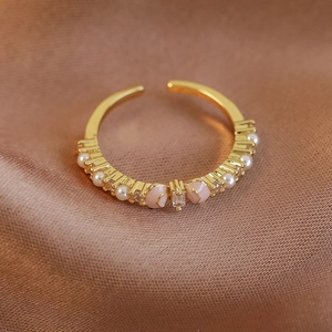 Detailansicht goldener Ring mit Zirkonia, Perlen und rosa Emaille auf Satin-Stoff