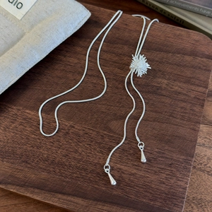 Detail of silver firework pendant on sleek snake chain over a wooden tray background