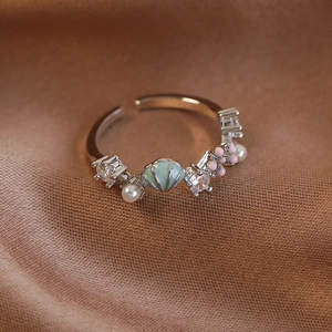 Detailaufnahme des Muschelrings mit Perlen und grüner Emaille auf braunem Stoff