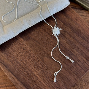 Detailed macro view of adjustable silver firework lariat necklace on a wooden tray