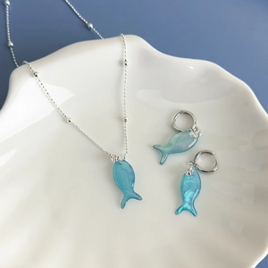 Vacation style blue colorful fish jewelry set with necklace and earrings on white shell plate