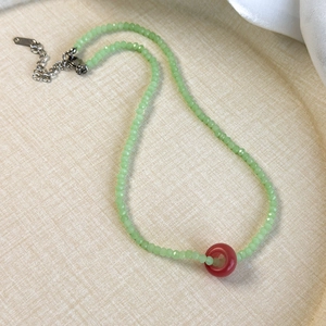 Close-up of green crystal beaded necklace with red ring pendant and metal lobster clasp