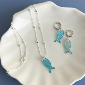 Ocean-themed silver necklace and blue fish earring set displayed in a white shell dish