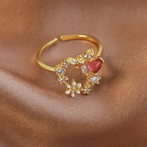 Close-up of golden adjustable ring with white flowers and red heart zircon on brown satin