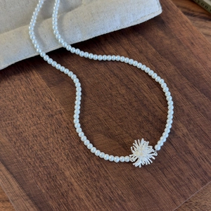Detail of silver firework pendant and white pearls on a textured wooden background
