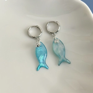 Close-up of blue iridescent fish earrings with silver hoops and sparkling zircon details