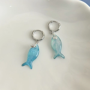 Macro detail of blue marble fish earrings on white ceramic tray with soft water ripples