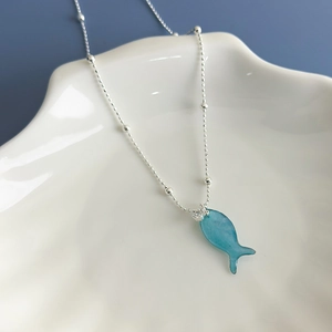 Close-up of blue fish pendant necklace on seashell tray with silver beaded chain