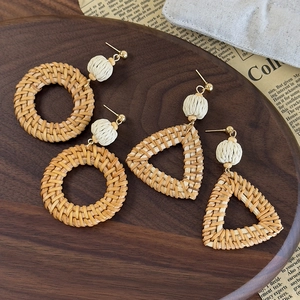 Bohemian rattan woven earrings in round and triangle shapes on a rustic wooden tray