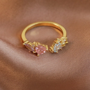 Détail d'une bague ouverte dorée ornée d'un cœur rose et de zircons colorés brillants