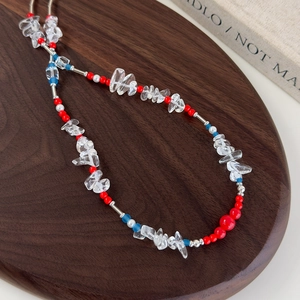 Ethnic style necklace with irregular crystal beads and red accents on a wooden plate