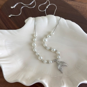 Elegant fishtail pearl necklace with silver chain displayed in a white seashell tray