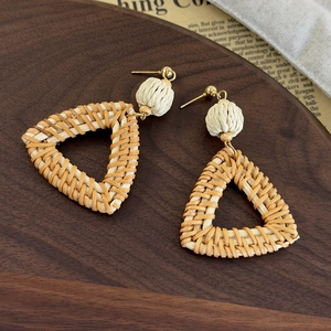 Close-up of bohemian triangle woven straw earrings with gold studs on a vintage tray