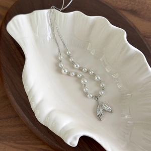 Close-up of a silver fishtail pearl necklace displayed inside a white shell dish
