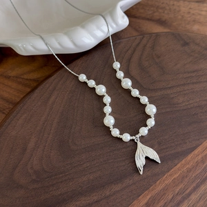 Elegant pearl necklace with silver mermaid tail pendant on a rustic wooden display