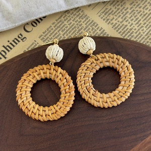 Detailed macro view of large round rattan woven bohemian earrings on a dark wood tray