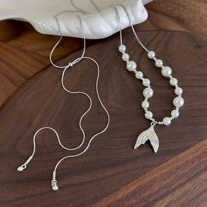 Close-up of pearl fishtail necklace on dark wood tray with shell decoration