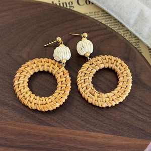 Detail of handmade bohemian rattan hoop earrings with beige woven beads on a wood tray